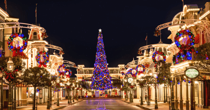 A beautiful night view of Main Street, U.S.A. at Magic Kingdom, adorned with festive Christmas lights and garlands, leading to a towering, brightly lit Christmas tree under a starry sky.